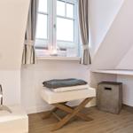 Schlafzimmer mit Fenster, Nachttisch, Stuhl und Schreibtisch.
