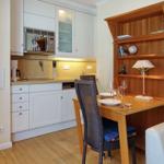 Kitchen with dining area and bookshelf. Wooden table, chairs, and white cabinets.