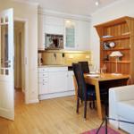 Apartment with kitchen, dining table, and sofa. Wooden floor and white furniture.