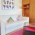 White sofa with cushions on red rug in front of wooden furniture.