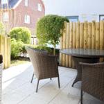 Terrace with round table and chairs, wooden fence, and green hedge in background.