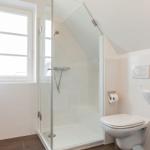 Shower area with glass enclosure, toilet, and sink in white bathroom fittings.