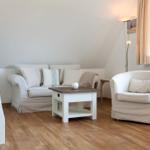 Living room with sofa, armchair, and table. Wooden floor and window with curtains.