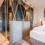 Schlafzimmer mit Bett, Holzboden und moderner Dusche mit Seilgestell.