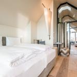 Schlafzimmer mit Doppelbett, Holzboden und Blick in Wohnbereich.
