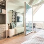 Schlafzimmer mit Balkon, Schrank und TV. Holzboden und große Fenster.