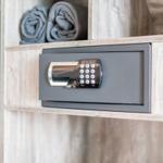 Ein digitaler Safe ist in einem Holzregal eingebaut, darüber liegen zwei gefaltete Handtücher.
