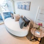 Rundes Sofa mit Kissen, kleiner Tisch und Wandheizung neben Glasfront.