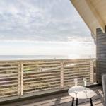Terrasse mit Meerblick, Tisch und zwei Gläser. Holzgeländer und graue Sitzgelegenheit.