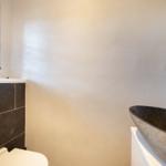 Bad mit Steinwaschbecken, Toilette und Fenster mit Jalousie.