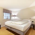Schlafzimmer mit Bett, Stuhl und Fenster. Holzboden und Stehlampe.