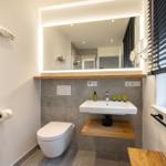 Bad mit Waschbecken, Toilette und Spiegel über Holzregal.