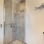 Dusche mit Glaswand, Wandhalterung und Fischdekoration.