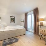 Schlafzimmer mit Bett, Schreibtisch und TV. Holzboden und große Fenster.