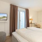 Schlafzimmer mit Doppelbett, Fernseher und Fenster mit Vorhängen.