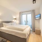 Schlafzimmer mit Bett, Fenster und Fernseher.