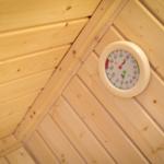 Sauna mit Holzwand und Temperatur-Feuchtigkeitsmessgerät an der Wand.