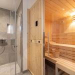 Dusche mit Glaswand und Sauna mit Holzbank und Eimer