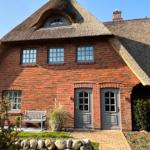 Red brick house with thatched roof and two entrances. Front garden with bench and stone wall.
