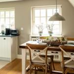 Dining area with wooden table, chairs, and windows. Kitchen with countertop and appliances.