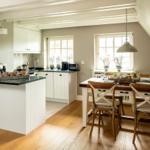 Kitchen with dining area, wooden floor, and white cabinets under sloped ceiling.