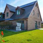 Haus mit Steinmauer, Terrasse und Garten. Weiße Gartenmöbel und Sonnenschirm.