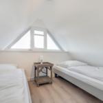 Zwei Betten unter Dachschrägen mit Fenster und Nachttisch.