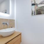 Waschbecken auf Holzunterschrank mit beleuchtetem Spiegel und Wandbild.