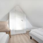 Zimmer mit zwei Betten, Stuhl und Tür unter Dachschrägen.