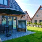 Terrasse mit Tisch, Stühlen und Sonnenschirm neben Strandkorb.