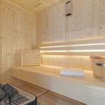 Sauna mit Holzbank, Thermometer und Eimer.