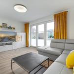 Wohnzimmer mit grauem Sofa, gelben Kissen und Fernseher.