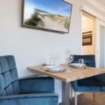 Essbereich mit Holztisch, blauen Stühlen und TV an der Wand.