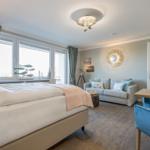 Schlafzimmer mit Bett, Sofa und Esstisch. Blaue Vorhänge und Wanddekoration.