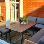 Terrasse mit Sitzgruppe, Tisch und Strandkorb vor rotem Backsteinhaus.