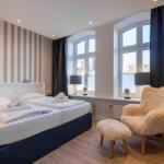 Schlafzimmer mit Bett, Fellstuhl und großen Fenstern.