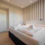 Schlafzimmer mit Doppelbett, Kleiderschrank und gestreifter Wand.
