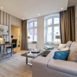 Wohnzimmer mit Sofa, Glas-Tisch und Fenstern mit Vorhängen.
