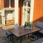 Terrasse mit Sitzgruppe, Tisch und Liegestuhl vor rotem Backsteinhaus.