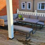 Terrasse mit Sitzgruppe, Tisch und Pflanzen an roter Backsteinwand.