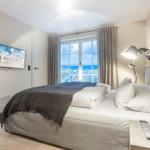 Schlafzimmer mit Blick aufs Meer, großes Bett, TV und Stehlampe.