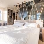 Schlafzimmer mit Bett, Holzmöbel und Dusche im Hintergrund.