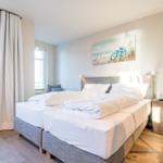Schlafzimmer mit Doppelbett, Fenstern und Wandbild.