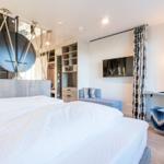 Schlafzimmer mit Bett, Kleiderschrank und TV. Blaue Sitzgelegenheit und dekorative Vorhänge.