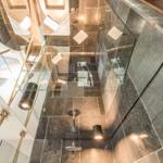Dusche mit Glaswand, dunklen Fliesen und modernen Lichtern.