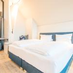 Schlafzimmer mit Doppelbett, Nachttisch und Blick auf Balkon.