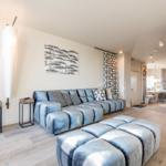 Wohnzimmer mit blauem Sofa und Fußhocker, moderner Beleuchtung und Wanddekoration.
