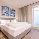 Schlafzimmer mit Doppelbett, Wandbildern und großem Fenster.