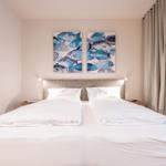 Schlafzimmer mit Doppelbett, Wandbildern und Vorhängen.