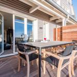 Terrasse mit Tisch und Stühlen, Blick ins Haus, Holzverkleidung und Sichtschutzwand.
